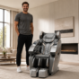 Tall man standing beside a silver Weltron massage chair in a modern living room, showing the size relationship
